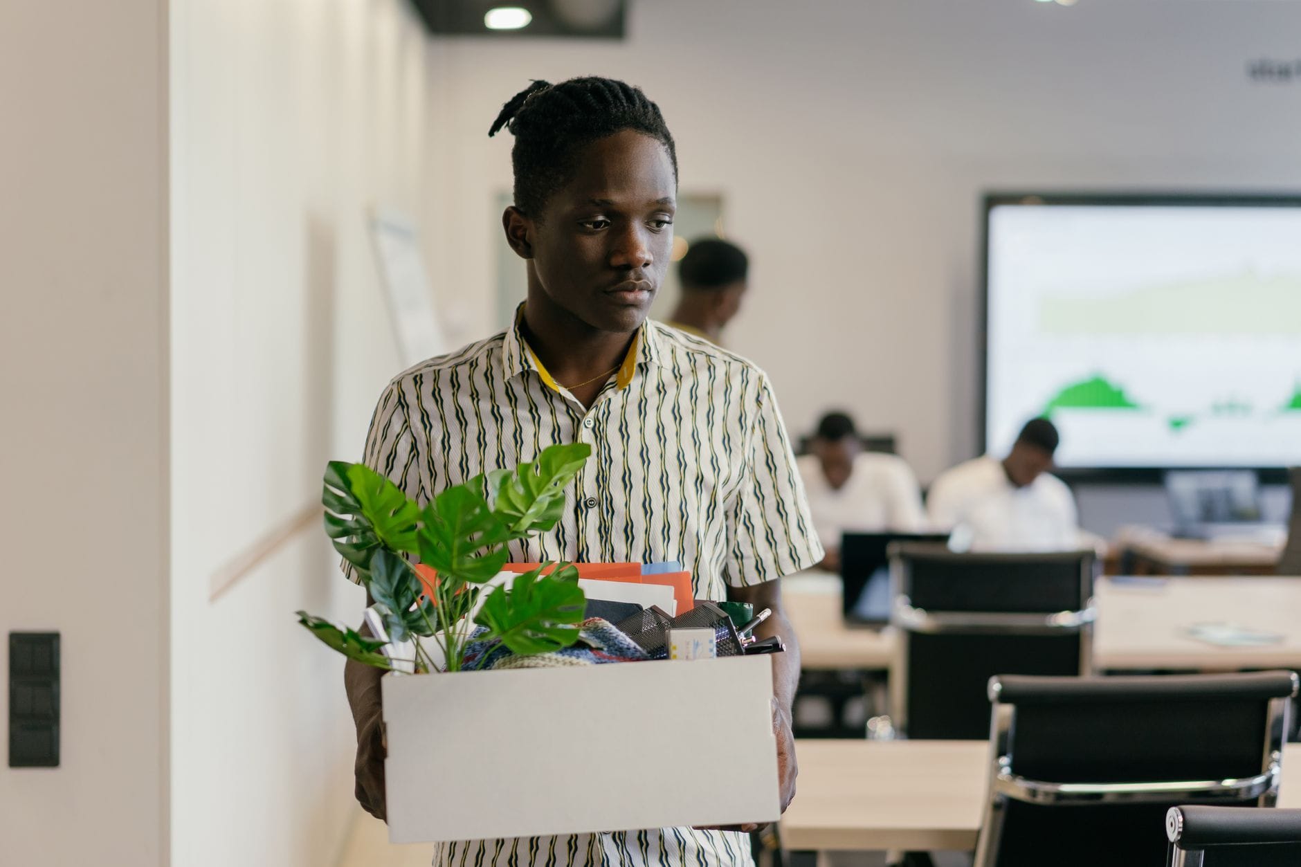 Młody mężczyzna z pudełkiem osobistych rzeczy odchodzi z biura Młody mężczyzna z pudełkiem osobistych rzeczy odchodzi z biura