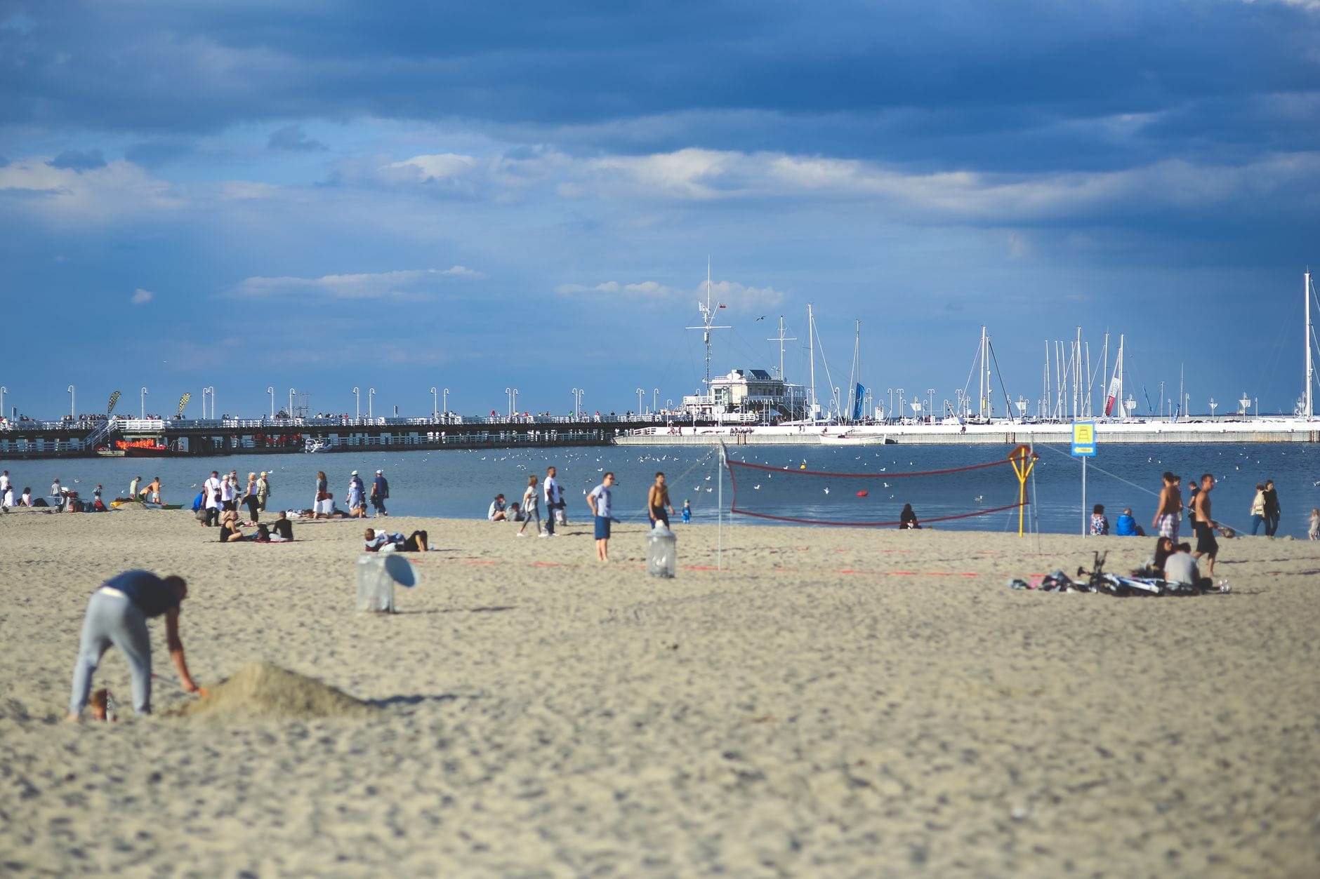 Plaża w Trójmieście z ludźmi grającymi w siatkówkę i łodziami w tle